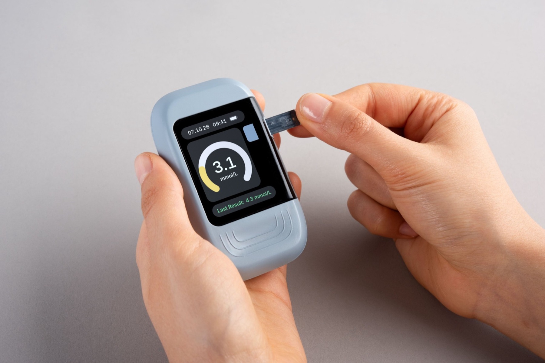 The Kali potassium monitor held in two hands while a test strip is inserted. Its screen shows a dial ready for a reading and the last result.
