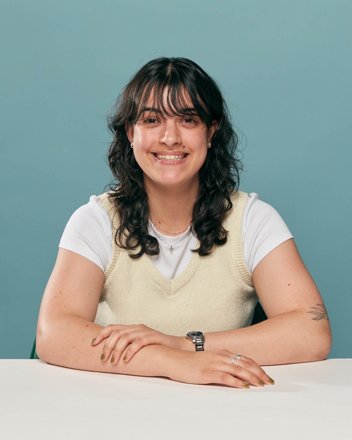 Sophia Kambouris sitting at a white table against a teal wall, smiling.